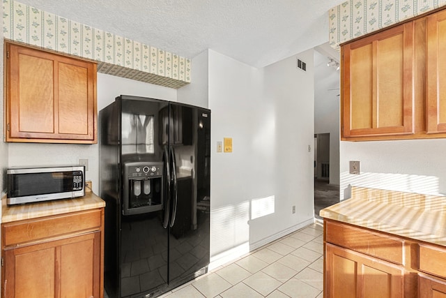 kitchen with light tile patterned floors, black fridge with ice dispenser, and a textured ceiling