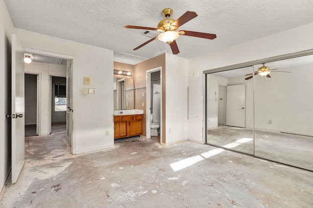 unfurnished bedroom with ceiling fan, a textured ceiling, a closet, and ensuite bath