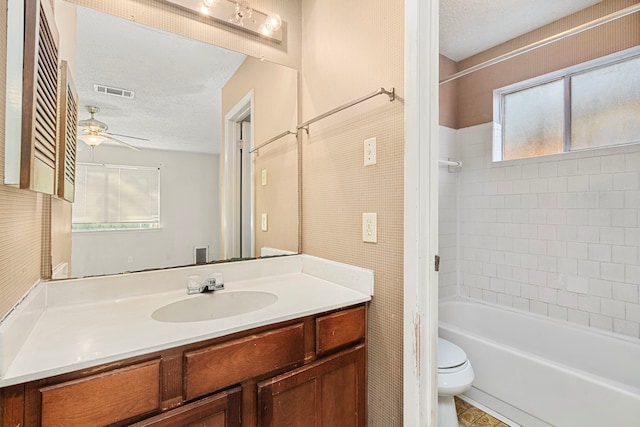 full bathroom with a textured ceiling, tiled shower / bath, vanity, toilet, and ceiling fan