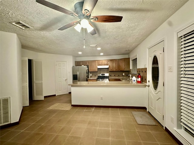 kitchen featuring stainless steel appliances, kitchen peninsula, ceiling fan, a textured ceiling, and tasteful backsplash