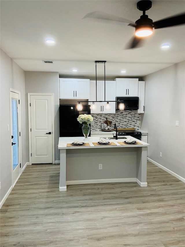 kitchen with black fridge, white cabinetry, light wood-type flooring, and decorative backsplash