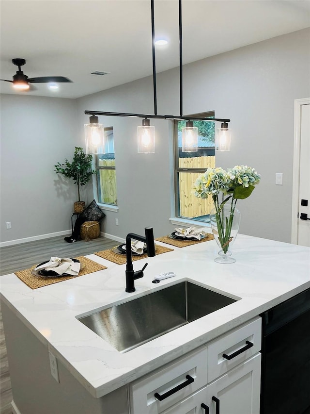 kitchen with sink, white cabinets, decorative light fixtures, light stone countertops, and a kitchen island