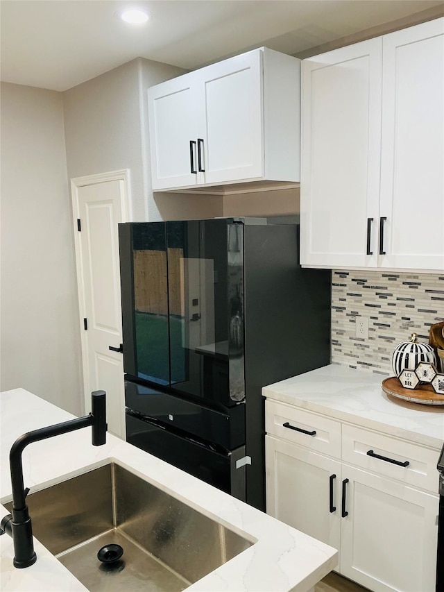 kitchen with sink, white cabinetry, black refrigerator, and tasteful backsplash