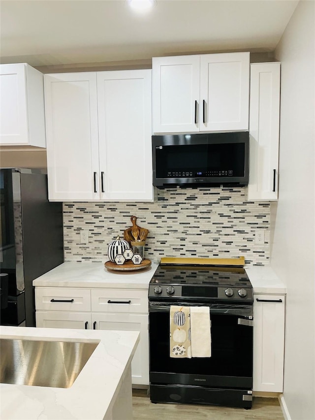 kitchen with appliances with stainless steel finishes, light hardwood / wood-style floors, backsplash, and white cabinetry