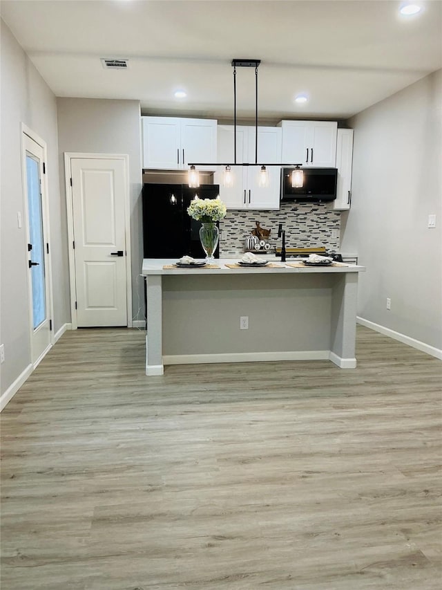 kitchen with white cabinetry, black fridge, tasteful backsplash, light hardwood / wood-style flooring, and pendant lighting