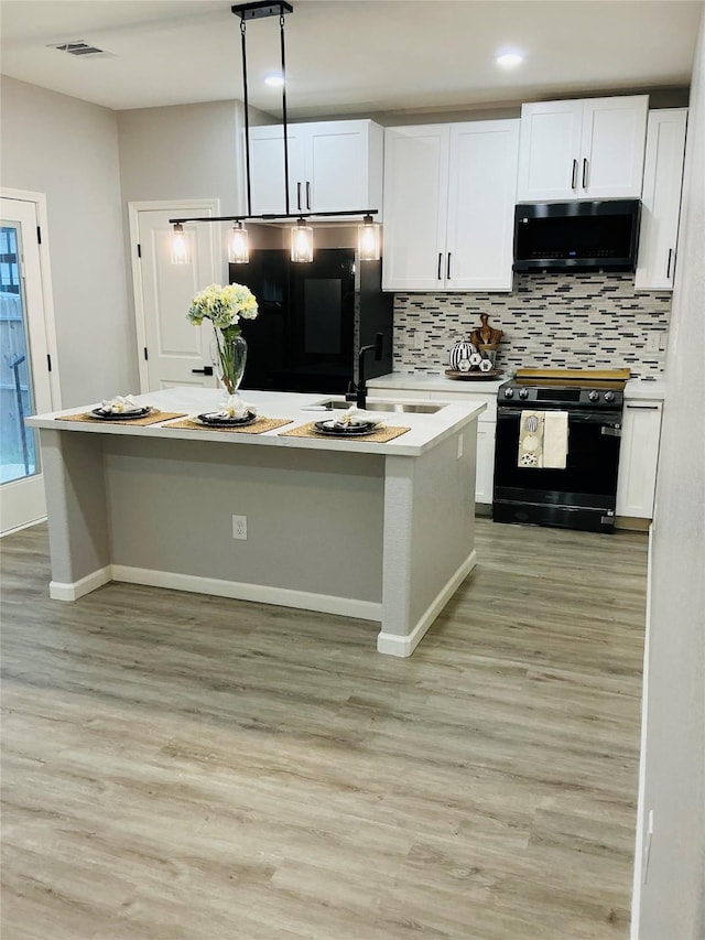 kitchen featuring sink, a kitchen island with sink, black appliances, and white cabinetry