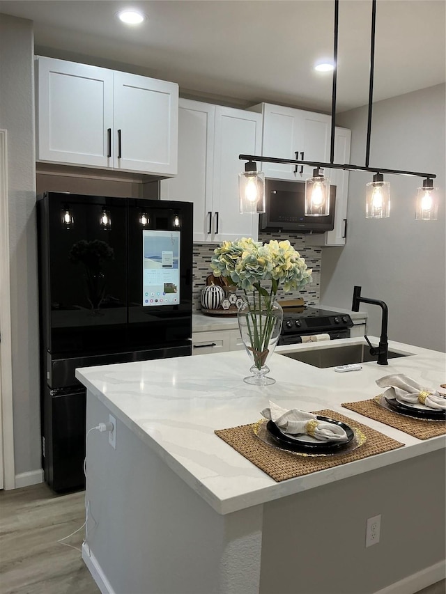 kitchen featuring black refrigerator, sink, white cabinetry, decorative light fixtures, and tasteful backsplash