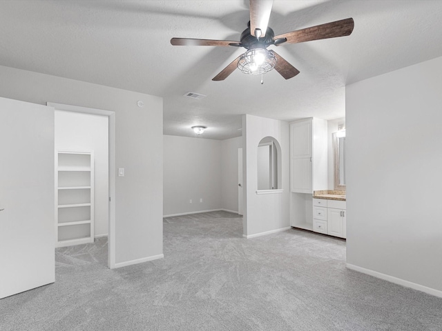 unfurnished bedroom with ensuite bath, a closet, light colored carpet, a walk in closet, and ceiling fan