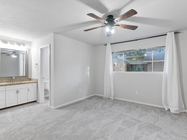 unfurnished bedroom featuring ensuite bath, a textured ceiling, ceiling fan, light carpet, and sink