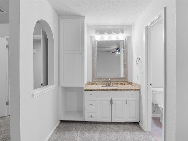 bathroom with ceiling fan, a textured ceiling, vanity, and toilet