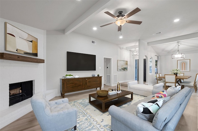 living room featuring ceiling fan with notable chandelier, a fireplace, light hardwood / wood-style floors, and vaulted ceiling with beams