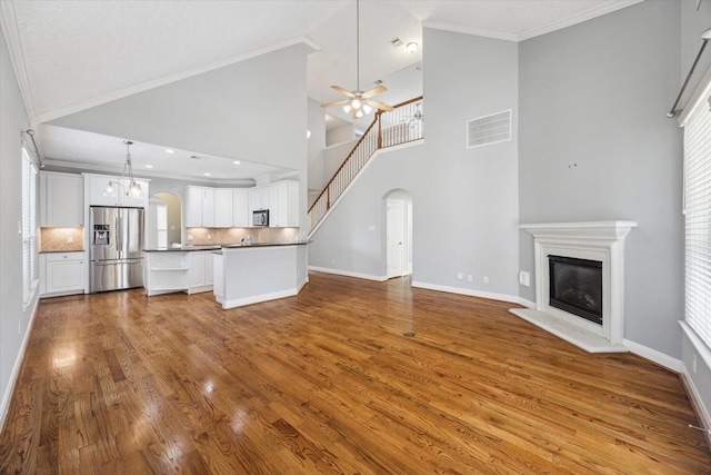 unfurnished living room with ceiling fan with notable chandelier, high vaulted ceiling, ornamental molding, and wood-type flooring