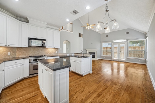 kitchen with kitchen peninsula, stainless steel appliances, decorative backsplash, a kitchen island, and ceiling fan with notable chandelier