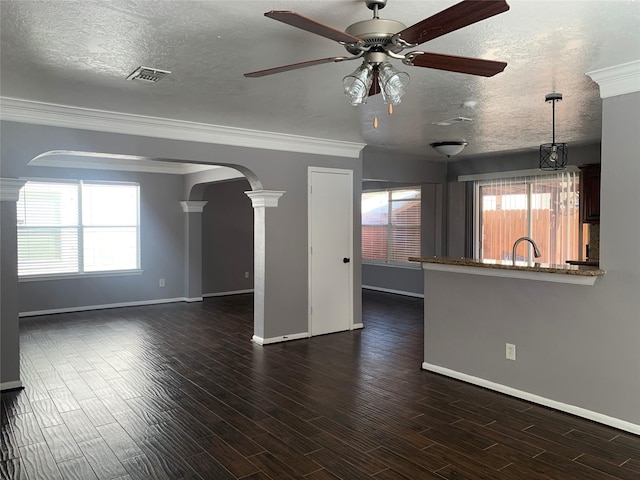 unfurnished living room with ceiling fan, a wealth of natural light, a textured ceiling, and decorative columns