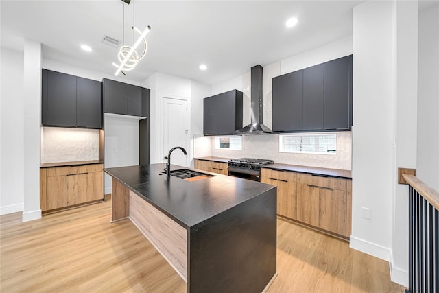 kitchen with a center island with sink, black range with gas stovetop, pendant lighting, wall chimney exhaust hood, and sink