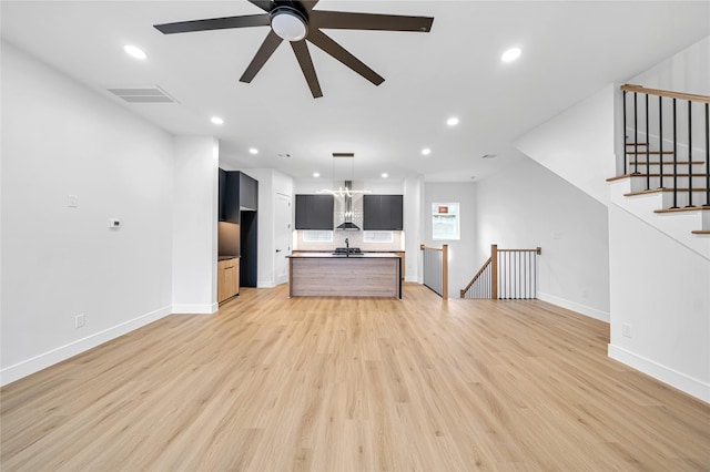 unfurnished living room with ceiling fan with notable chandelier and light hardwood / wood-style floors