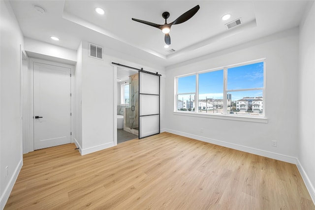 unfurnished bedroom with ensuite bath, a raised ceiling, and a barn door