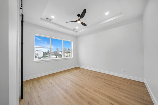 unfurnished room with ceiling fan, light hardwood / wood-style flooring, and a tray ceiling