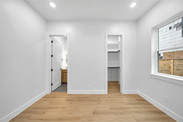 unfurnished bedroom featuring ensuite bath, light wood-type flooring, a closet, and a spacious closet