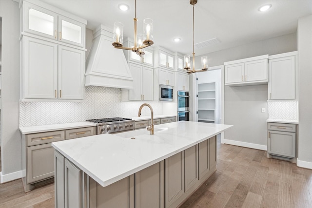 kitchen featuring hanging light fixtures, a kitchen island with sink, white cabinetry, and custom range hood