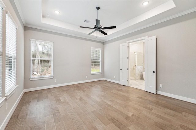 unfurnished bedroom featuring ceiling fan, ensuite bathroom, a raised ceiling, and multiple windows