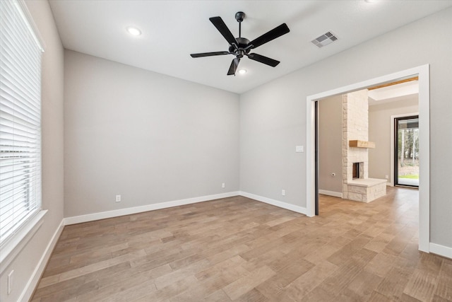 empty room featuring light wood-type flooring, ceiling fan, and a stone fireplace