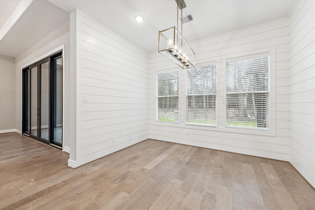 unfurnished dining area with wood walls, a notable chandelier, and light wood-type flooring