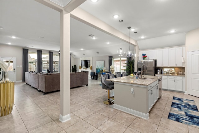 kitchen featuring pendant lighting, light stone counters, an island with sink, white cabinets, and vaulted ceiling