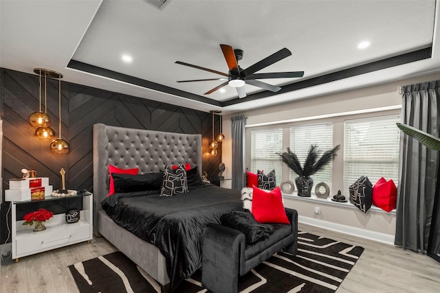 bedroom featuring ceiling fan, a raised ceiling, and light hardwood / wood-style floors