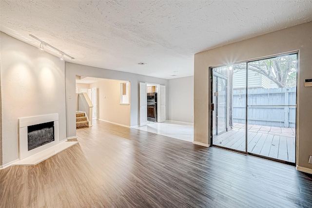 unfurnished living room with track lighting, wood-type flooring, a textured ceiling, and heating unit