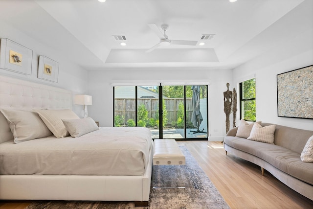 bedroom featuring hardwood / wood-style flooring, ceiling fan, access to outside, and a tray ceiling