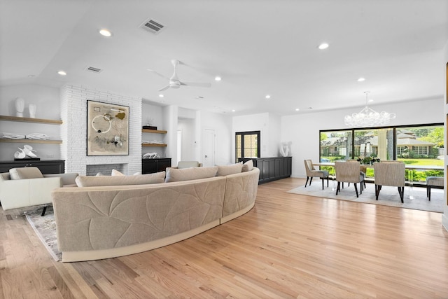 living room with ceiling fan with notable chandelier, a fireplace, light hardwood / wood-style floors, and lofted ceiling