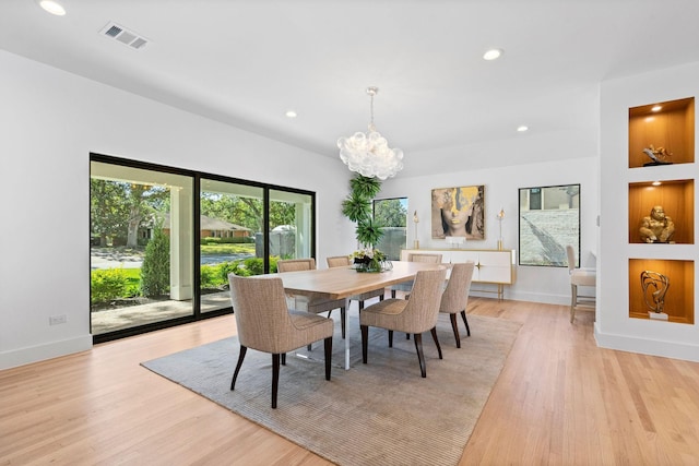 dining room featuring built in shelves, an inviting chandelier, and light hardwood / wood-style flooring