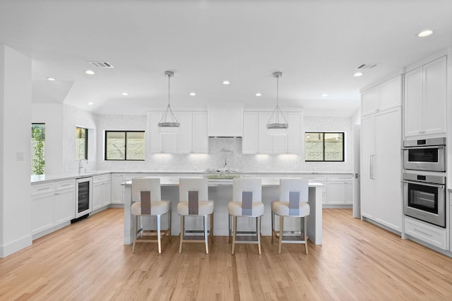 kitchen featuring white cabinetry, decorative light fixtures, stainless steel double oven, and a breakfast bar area