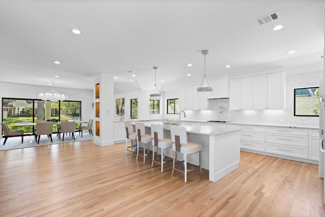 kitchen with a kitchen breakfast bar, a center island with sink, decorative light fixtures, and white cabinetry