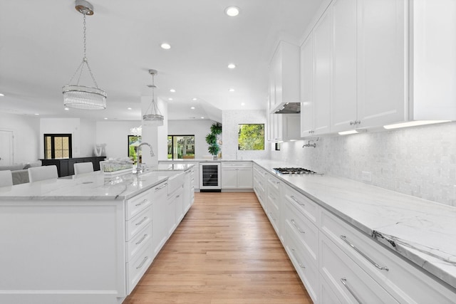 kitchen with decorative light fixtures, an inviting chandelier, wine cooler, white cabinetry, and a large island with sink