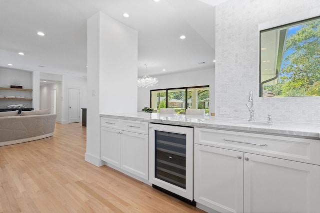 kitchen with white cabinets, light hardwood / wood-style flooring, light stone countertops, and wine cooler