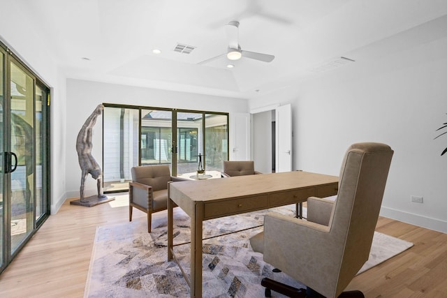 dining room with a raised ceiling, ceiling fan, and light hardwood / wood-style flooring