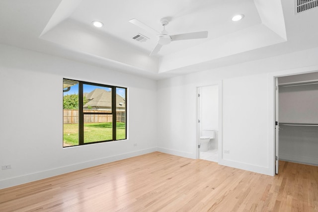 unfurnished bedroom featuring ensuite bath, a raised ceiling, ceiling fan, and light hardwood / wood-style floors