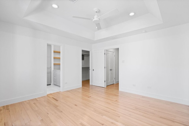 spare room with ceiling fan, light wood-type flooring, and a raised ceiling