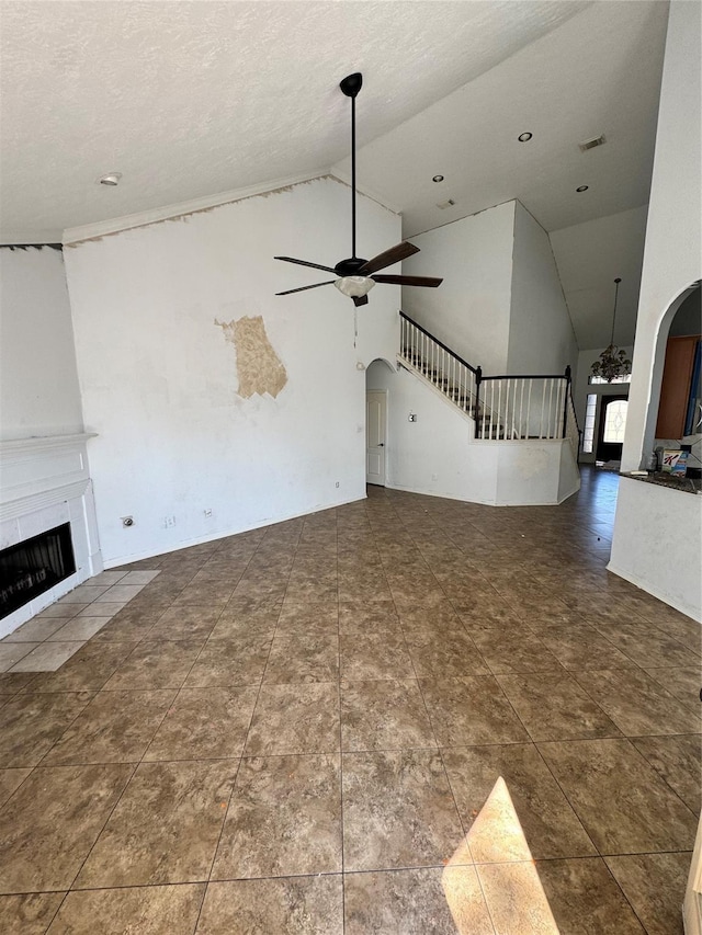 unfurnished living room featuring a tiled fireplace, ceiling fan, dark tile patterned floors, high vaulted ceiling, and a textured ceiling