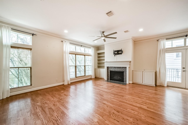 unfurnished living room with ceiling fan, crown molding, a healthy amount of sunlight, light wood-type flooring, and built in shelves