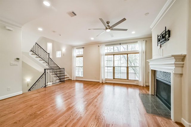 unfurnished living room with ceiling fan, a tiled fireplace, crown molding, and hardwood / wood-style flooring