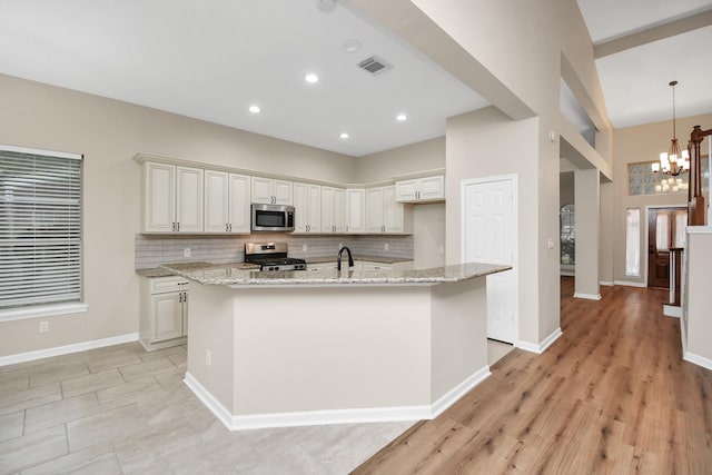 kitchen featuring stainless steel appliances, an island with sink, light stone counters, and hanging light fixtures