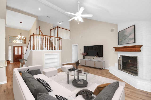 living room with light hardwood / wood-style flooring, built in shelves, high vaulted ceiling, ceiling fan with notable chandelier, and a fireplace