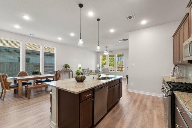 kitchen with a kitchen island with sink, stainless steel appliances, ceiling fan, pendant lighting, and sink