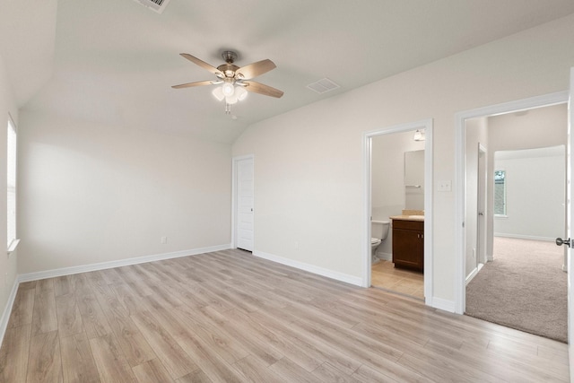 unfurnished bedroom with ensuite bathroom, ceiling fan, vaulted ceiling, and light wood-type flooring