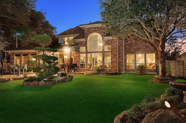 back house at dusk featuring a yard and a patio area