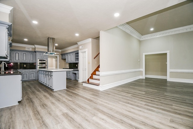 kitchen with stainless steel double oven, a kitchen island, island exhaust hood, sink, and gray cabinets