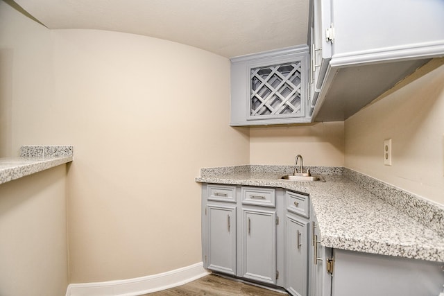 kitchen with light stone countertops, sink, wood-type flooring, and gray cabinets